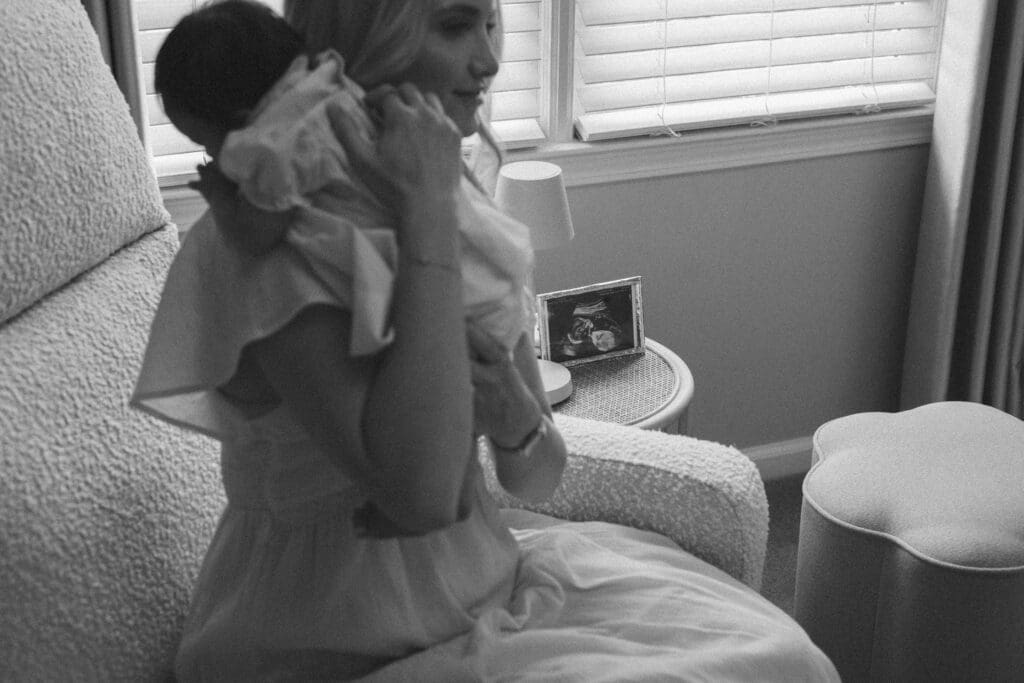 documentary styled moment of mother hold daughter during inhome newborn family session, in black and white image with the sonogram in the background. by georgia family and wedding photographer kattie jackson 